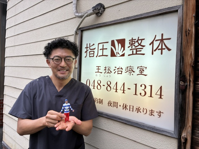 王拯治療室の看板前で、フィギュアを手にのせたようす