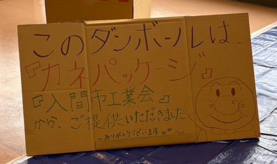 「このダンボールは『カネパッケージ』『入間市工業会』から、ご提供いただきました ありがとうございます」と書かれた手書きの看板